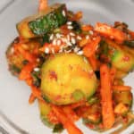 Sliced cucumbers mixed with Korean red pepper flakes in a clear bowl with carrots