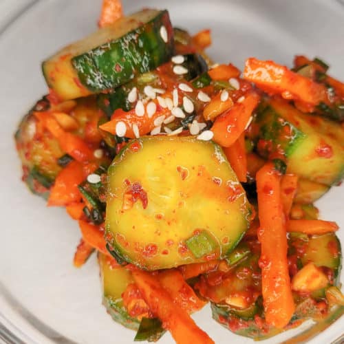Sliced cucumbers mixed with Korean red pepper flakes in a clear bowl with carrots