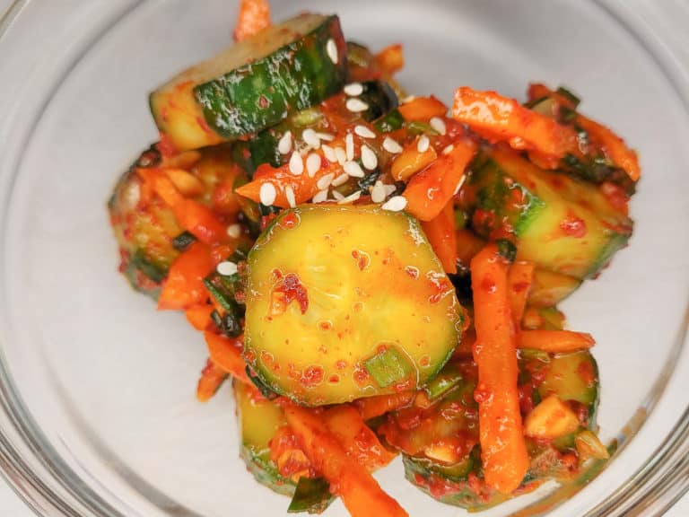 Sliced cucumbers mixed with Korean red pepper flakes in a clear bowl with carrots