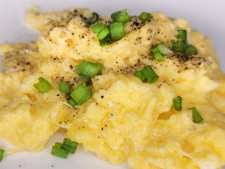 A closeup of creamy scrambled eggs with green onions on a white plate