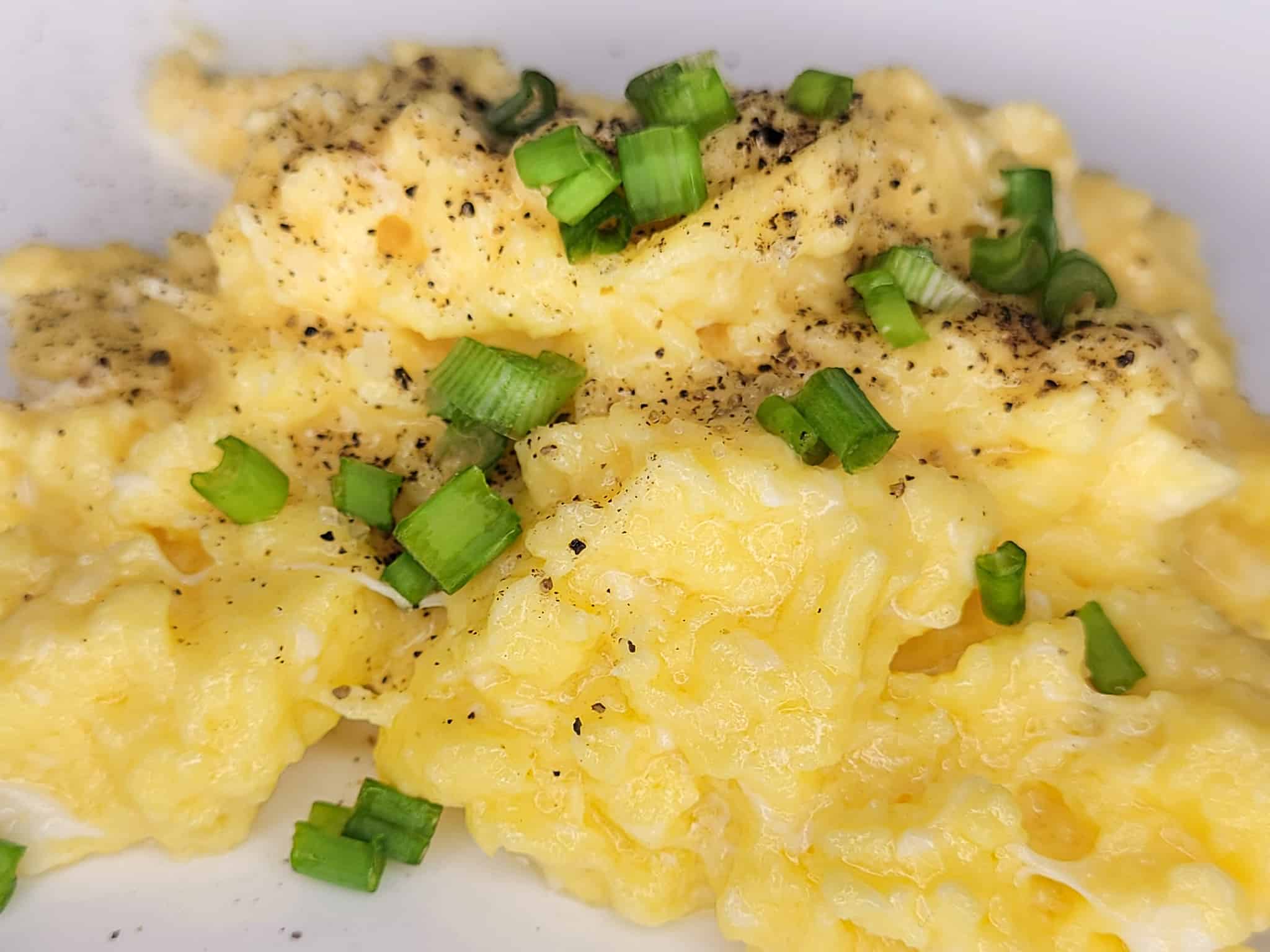 A closeup of creamy scrambled eggs with green onions on a white plate