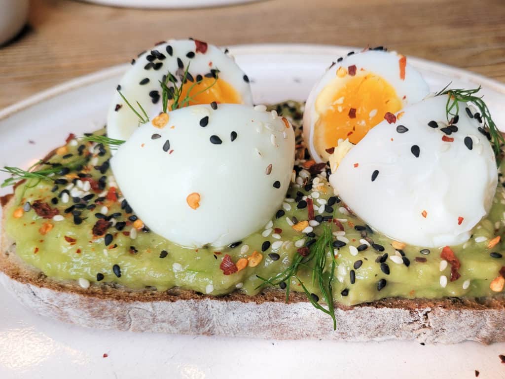 A slice of bread with mashed and seasoned avocados and soft boiled eggs on top