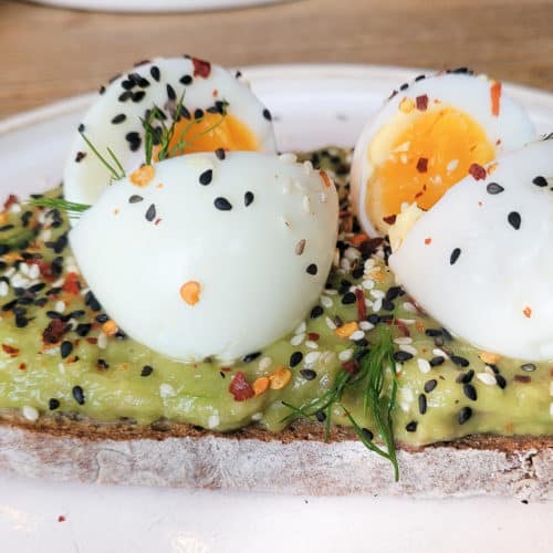 A slice of bread with mashed and seasoned avocados and soft boiled eggs on top