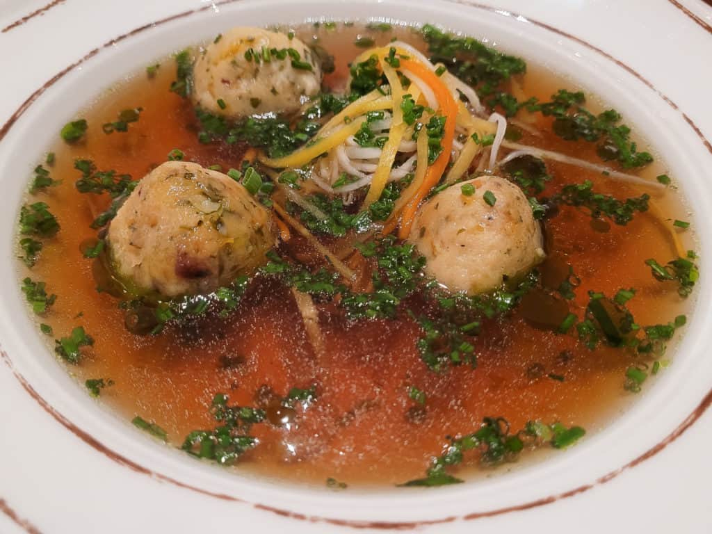 A bowl of clear broth soup with balls of bread dumplings
