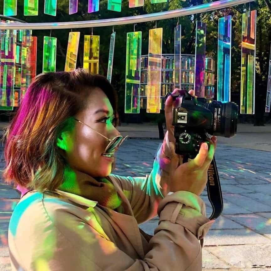 Woman standing sideways and wearing sunglasses holding a camera