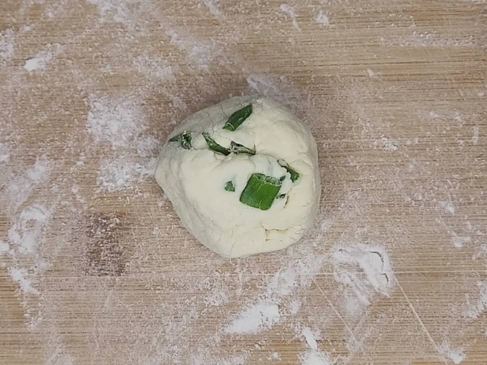 An overhead view of a dough ball with pieces of green onions