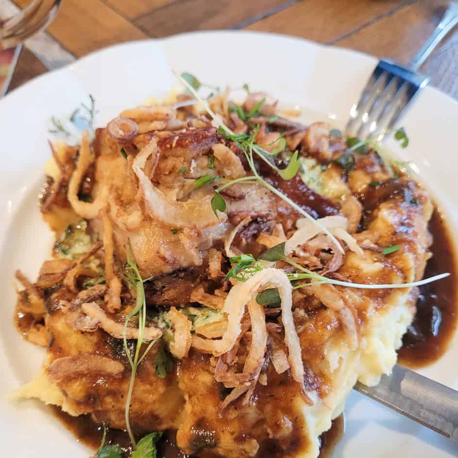 A plate of slow roasted pork belly topped with crispy onions set on top of mashed potatoes