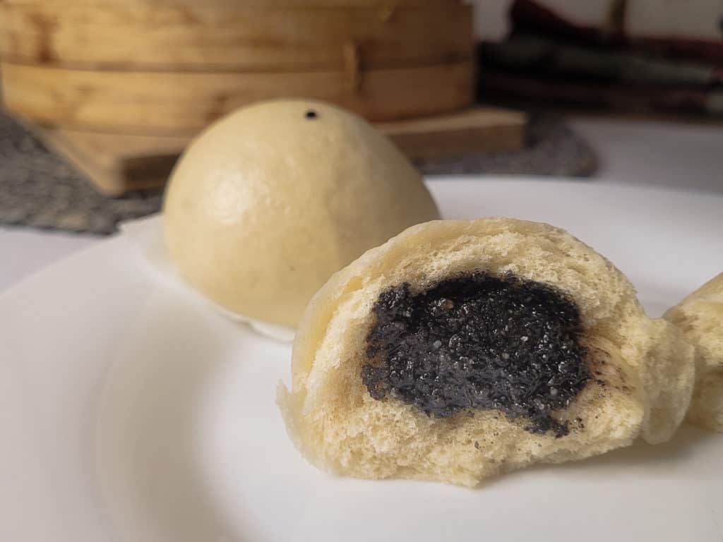 Closeup black sesame seed bun on plate with steamer basket in the background