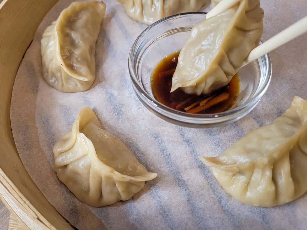 A dumpling being dipped in a soy sauce and vinegar