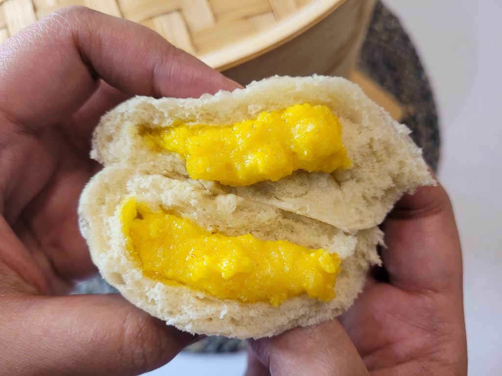 Salted egg yolk custard in a white bun held by hands