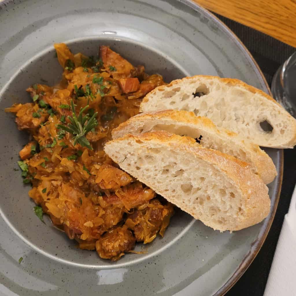 Polish stew in a gray bowl next to some slices of bread.