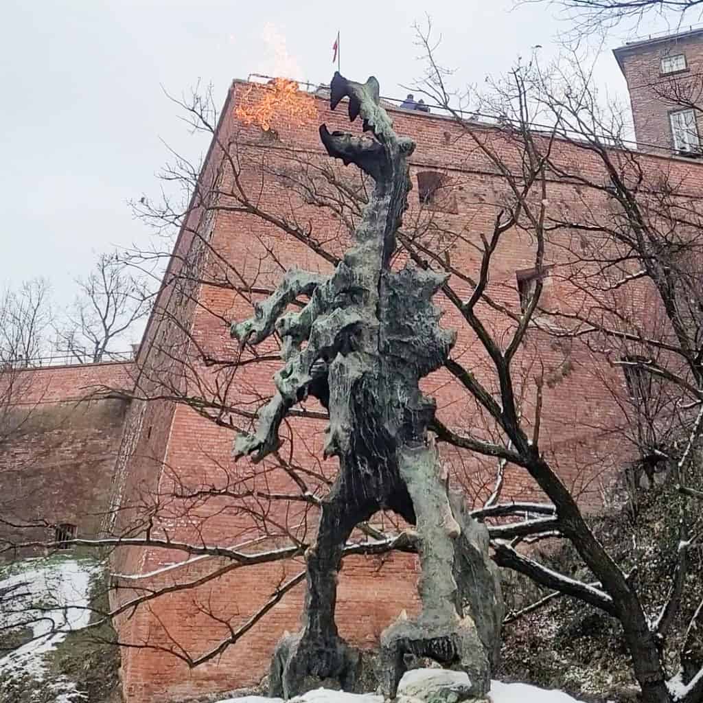 A statue of a dragon breathing fire in action in front of the Wawel Castle In Krakow, Poland