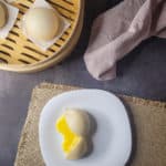 Overhead shot of salted egg yolk lava bun next to a bamboo steamer of other buns
