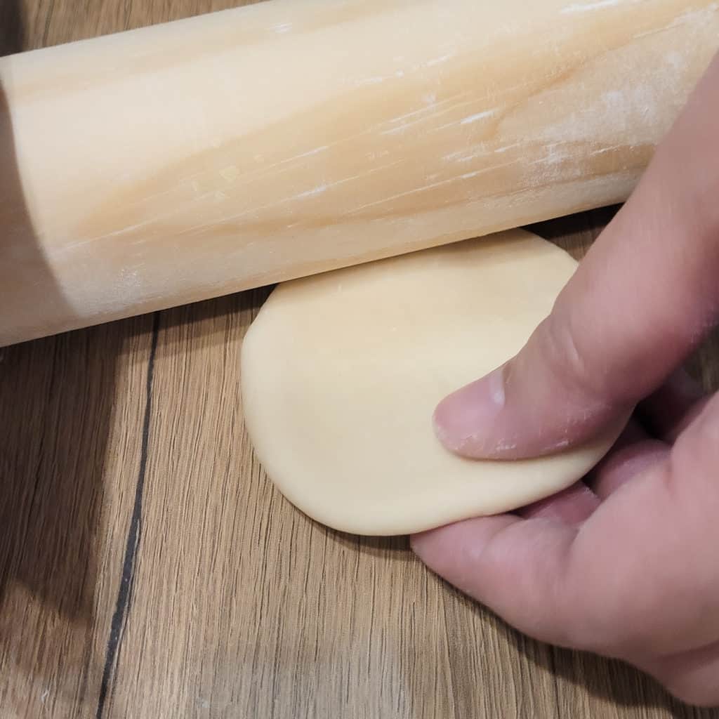 Dough held by a hand and being flattened with a rolling pin