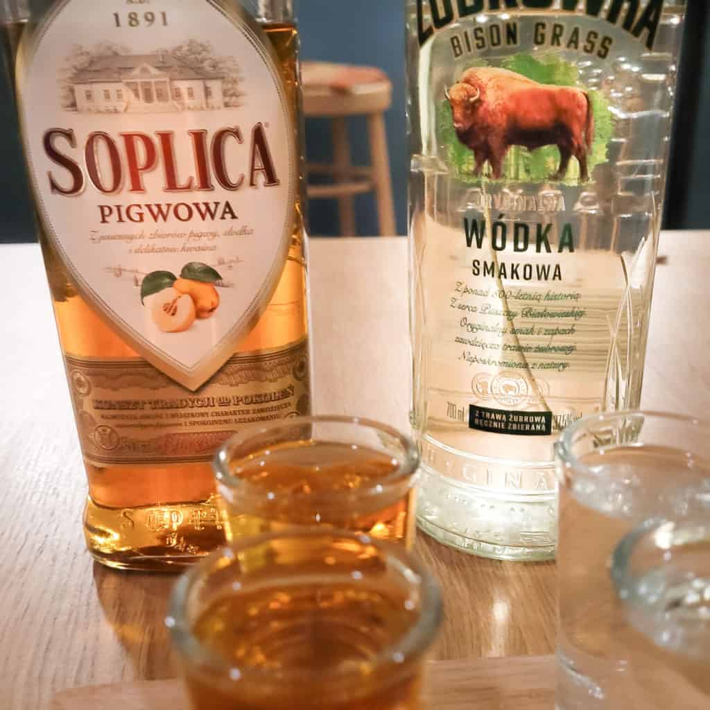 Two bottles of vodka with shot glasses in the foreground on a wooden table