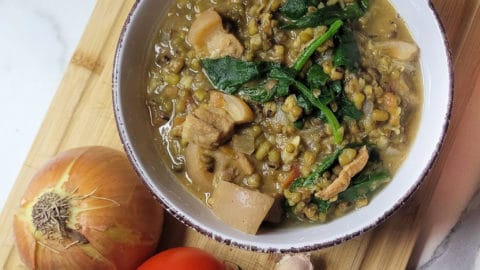 Filipino mongo in a white bowl next to an onion, tomato and some garlic cloves
