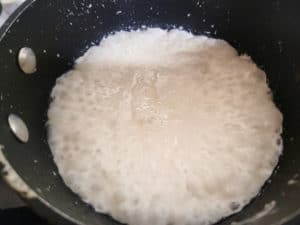 Closeup of coconut cream boiling in a small black pot