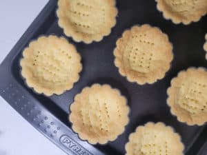 Baked tart shells on a dark gray baking sheet