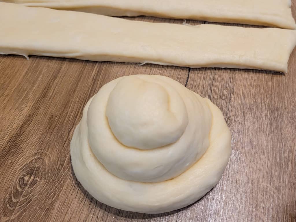Rolled bun that looks like a cinnamon roll next to strips of dough