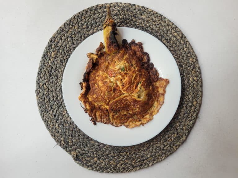 Fried eggplant with vegetables on a white plate set on a blue round mat