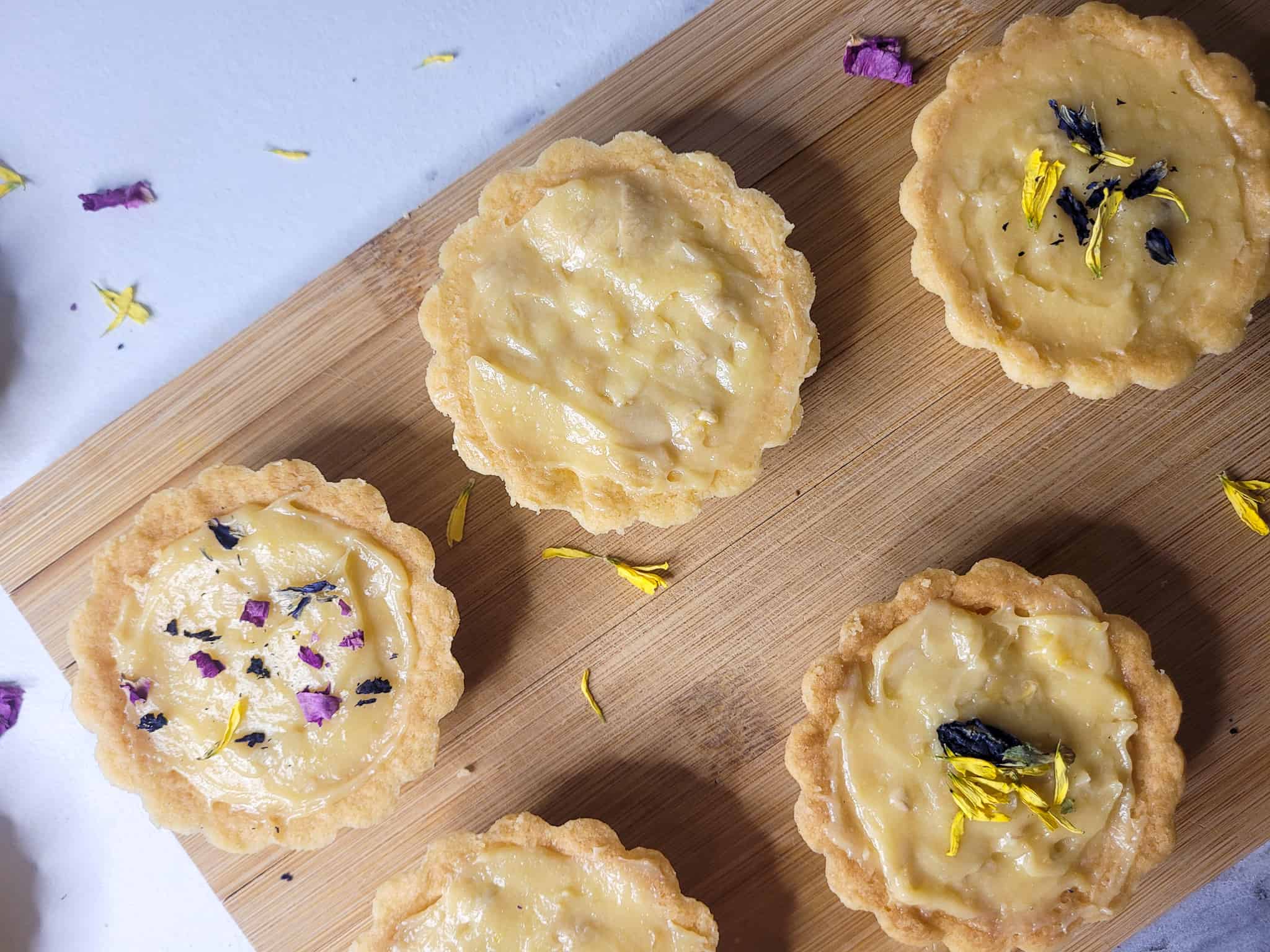 Cashew yema tarts with blue and yellow flower petals on a wood cutting board