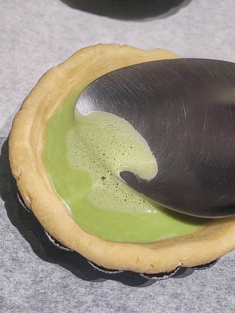 Bubbles removed with silver spoon in a matcha Portuguese egg tart