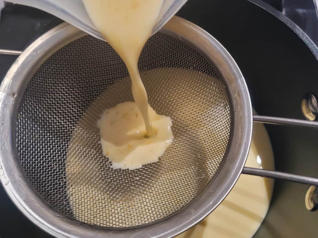 Egg mix poured through metal sieve into pot