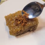 A silver spoon dropping some latik on top of a slice of biko or baked sticky rice