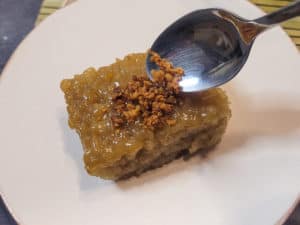 A silver spoon dropping some latik on top of a slice of biko or baked sticky rice