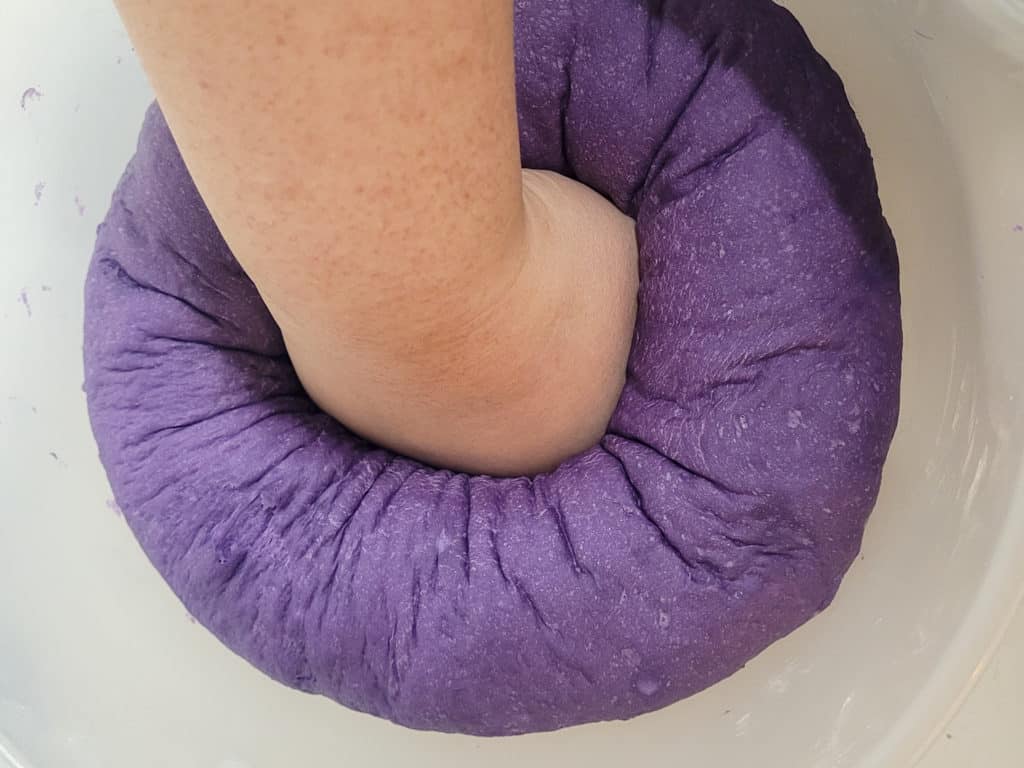 A hand punching out gas from proofed ube pandesal dough