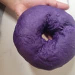 A hand holding purple dough shaped like a donut