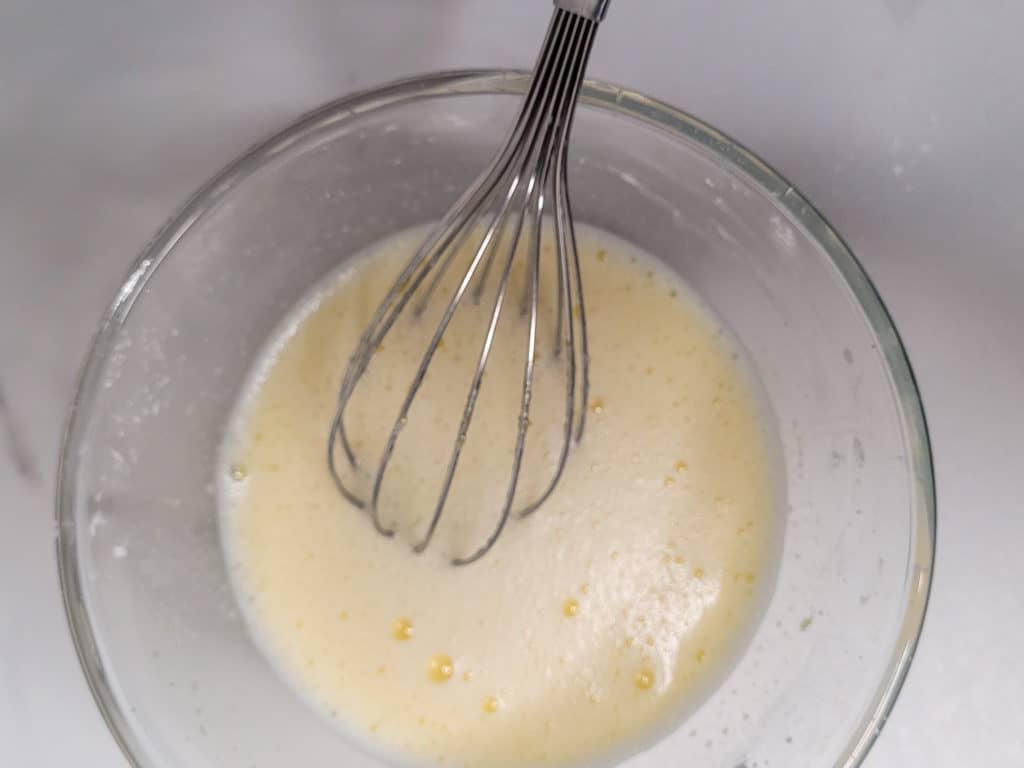 A mix of egg yolk with whisk in clear bowl