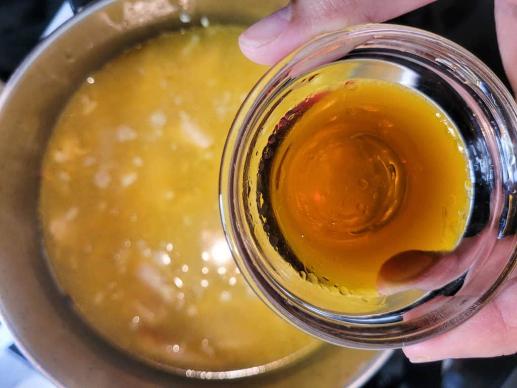 Fish sauce in a small clear bowl in above a pot of porridge