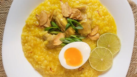 Overhead view of arroz caldo in a square white bowl on a weaved placemat