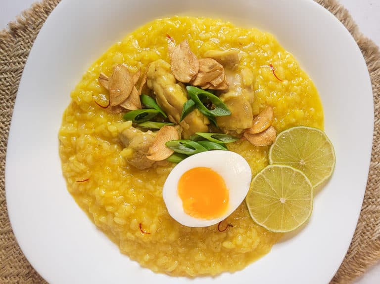 Overhead view of arroz caldo in a square white bowl on a weaved placemat