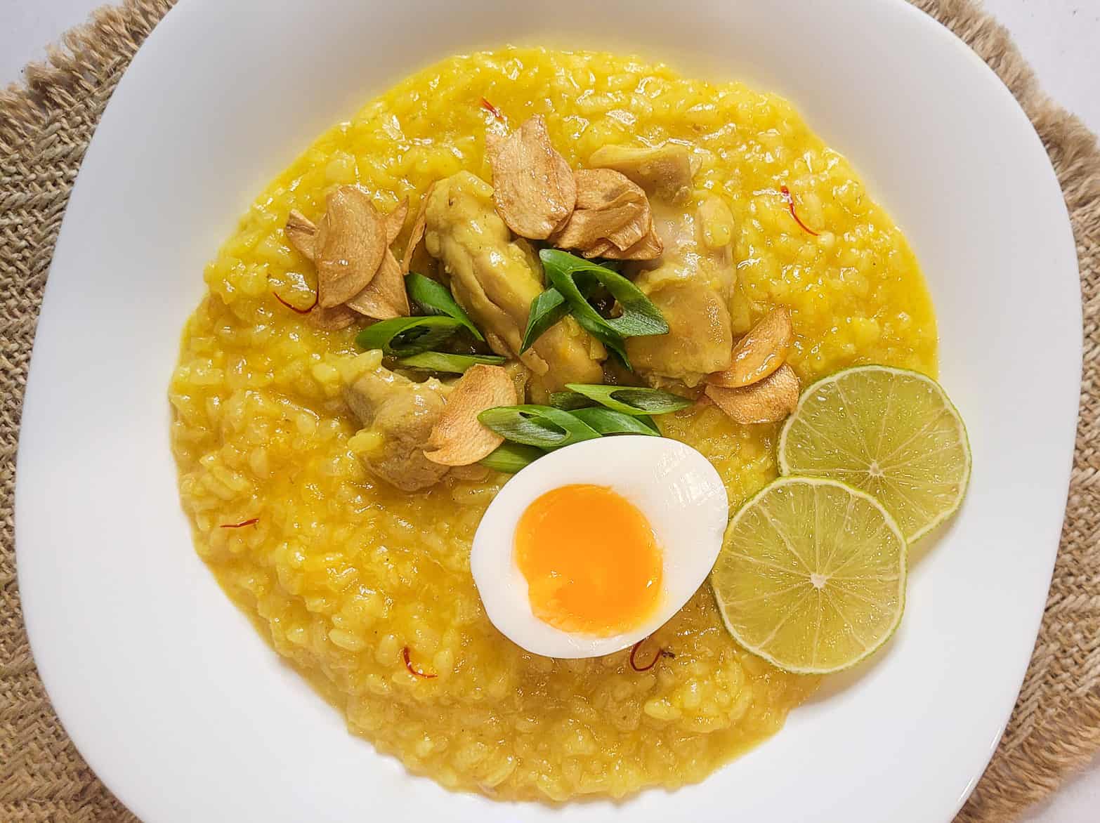 Overhead view of arroz caldo in a square white bowl on a weaved placemat