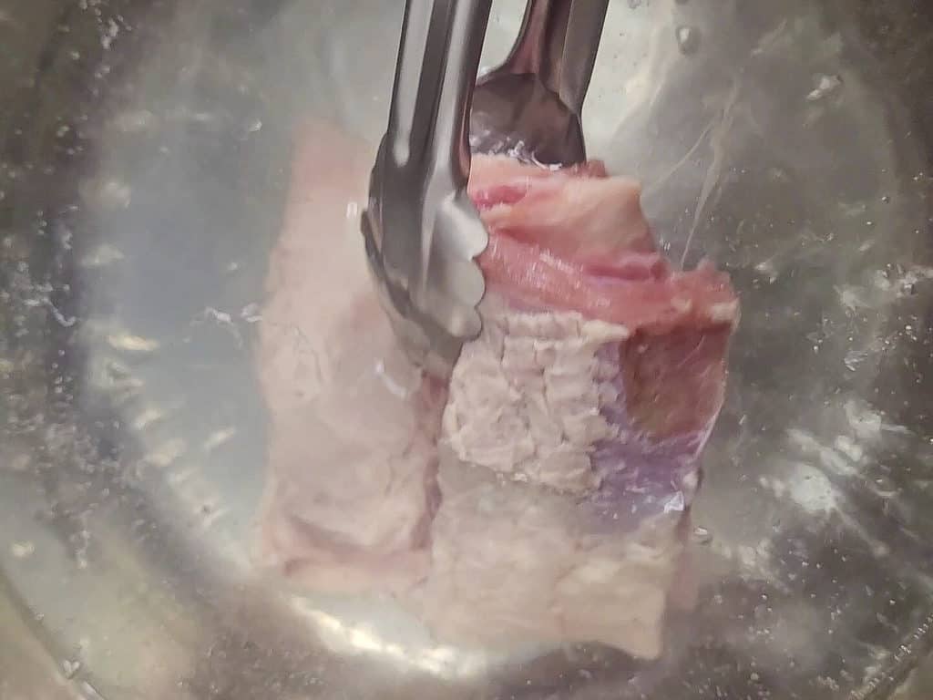 Tongs placing beef ribs in boiling water