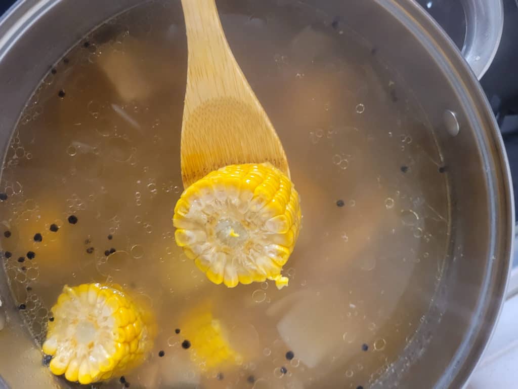 A wooden spoon with a piece of corn on the cob above a pot