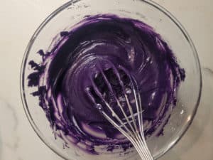 Ube cinnamon roll frosting in a clear bowl