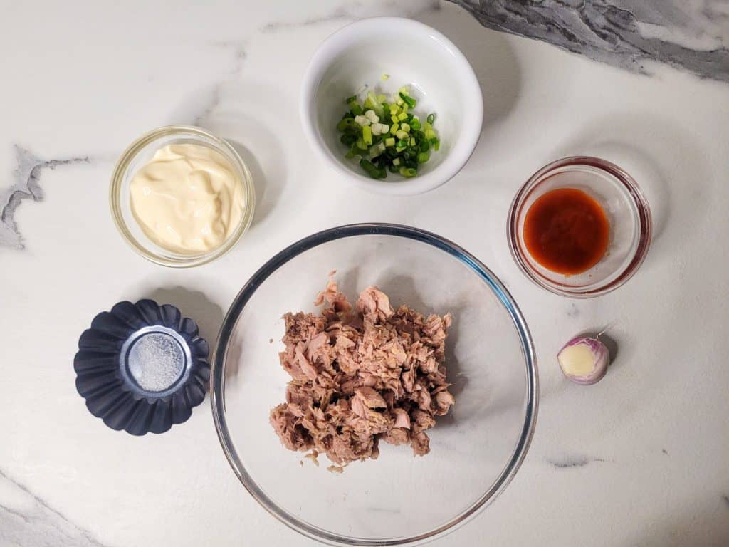 Tuna in a clear bowl surrounded by other ingredients in smaller bowls