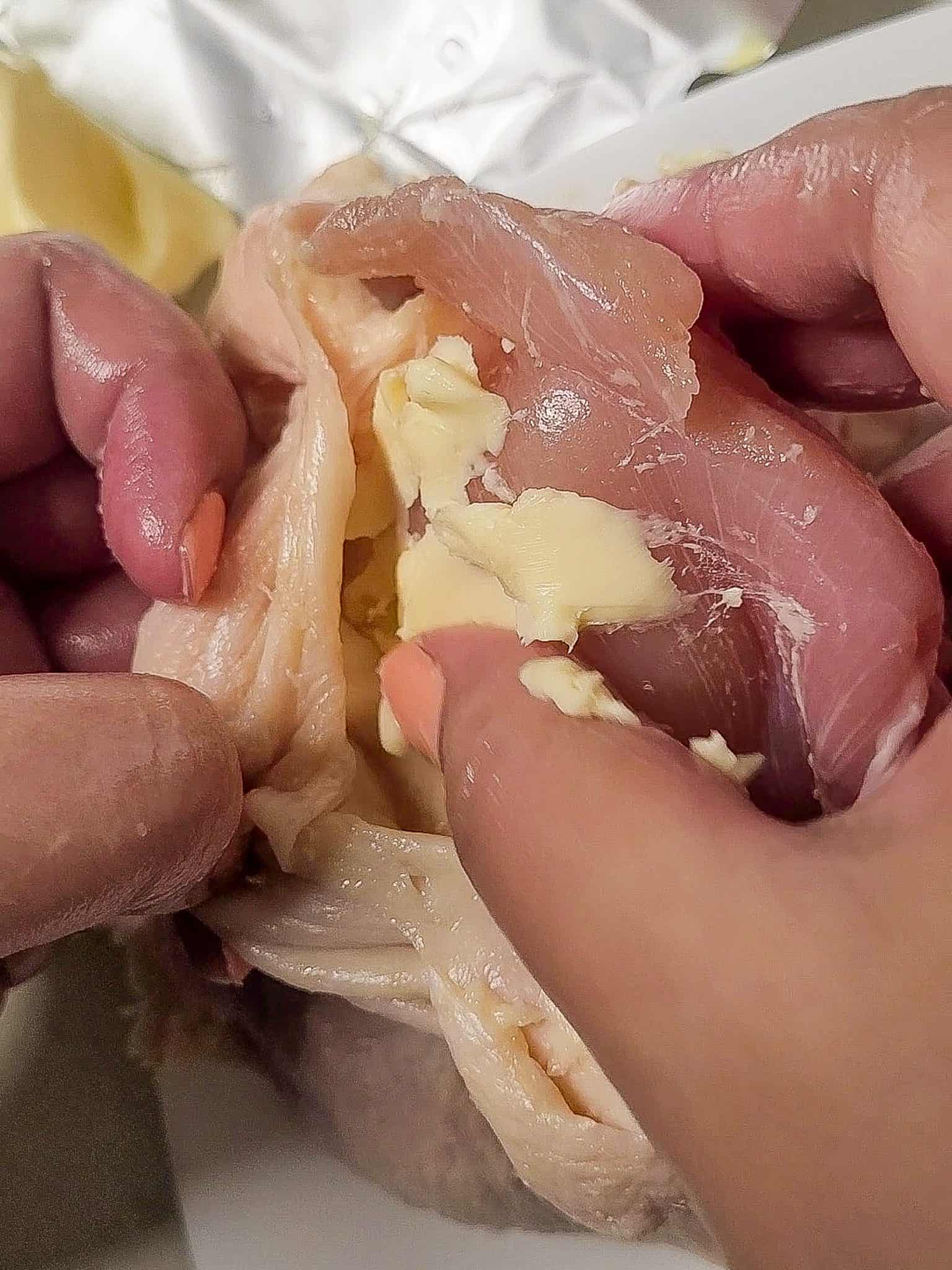Adding butter under chicken skin with hands