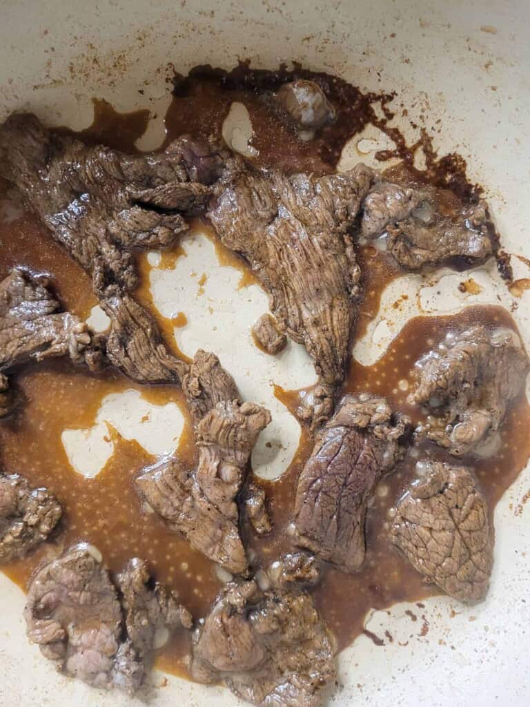 Beef cooking in a pan with sauces