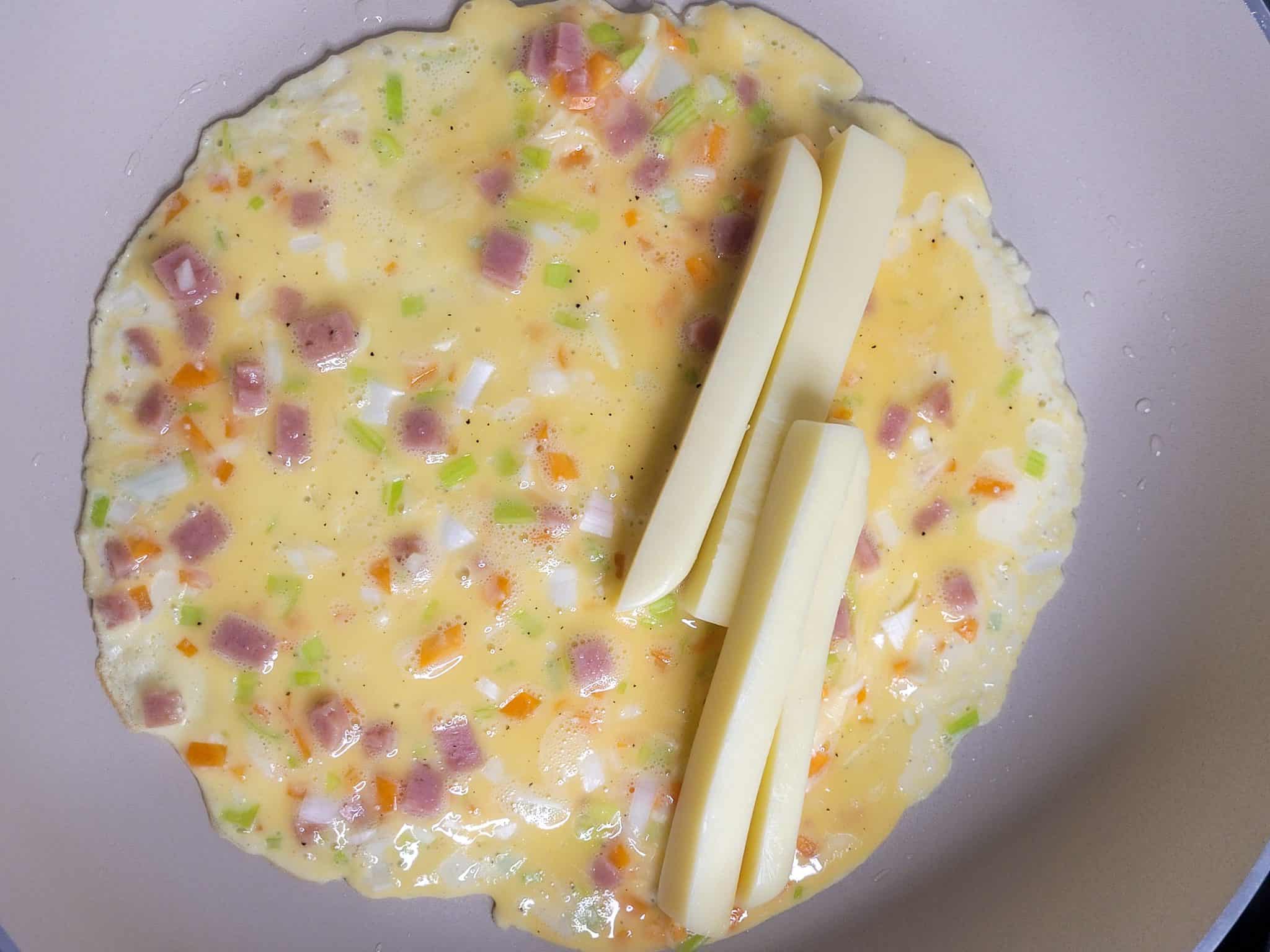 Raw egg in pan with vegetables and cheese sticks