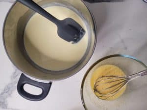 A pot with melted chocolate next to a bowl with whisked egg yolks