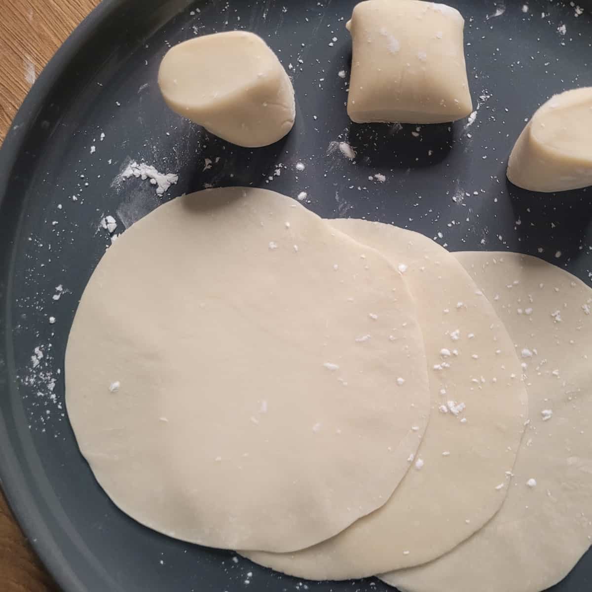 Flattened dumpling wrappers and pieces of dumpling wrappers on a gray plate