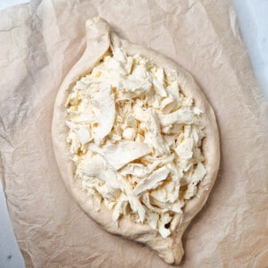 Shredded cheese on top of raw dough shaped like a boat