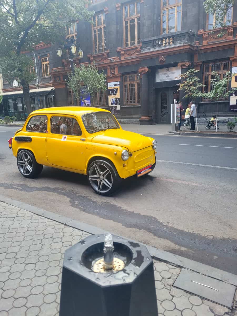 Yellow car behind a water fountain on the street
