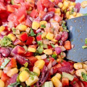 Closeup of cowboy caviar (mixed corn pico de gallo) with a gray spatula