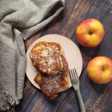 Apple fritters topped with powdered sugar with apples next beside it