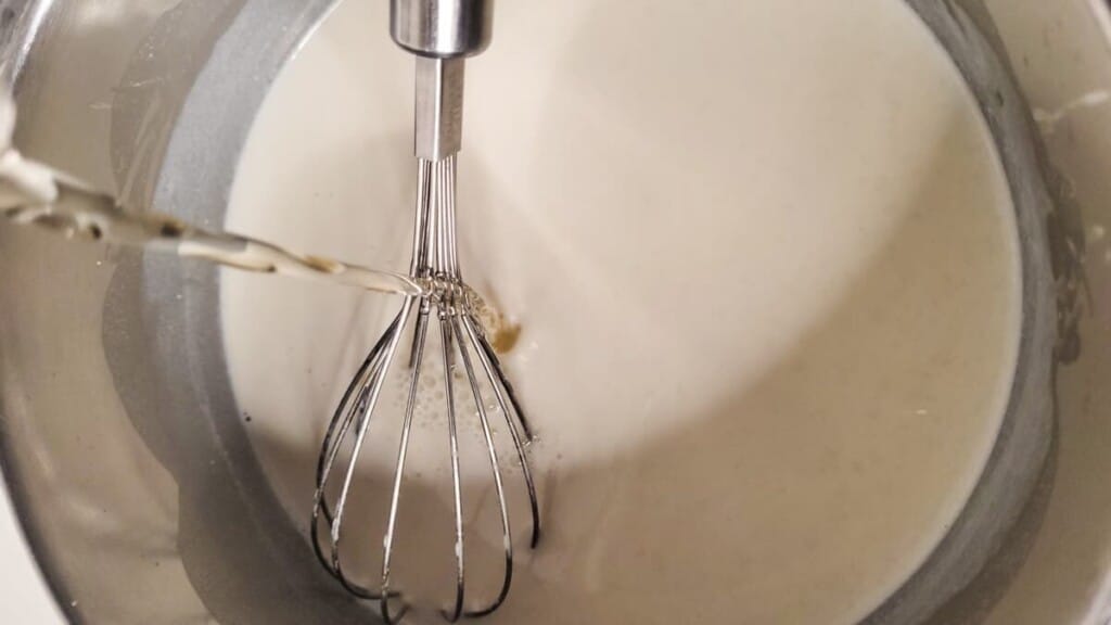 Clear liquid being poured into a silver pot with a whisk